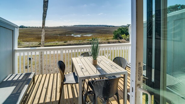 Um deck de madeira com mesa e cadeiras, com vista para uma paisagem pantanosa.