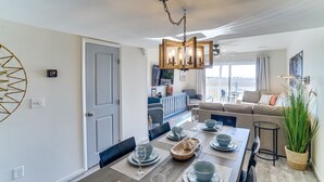 Uma sala de jantar com uma mesa de madeira posta para quatro pessoas, um candelabro e vista para uma varanda.