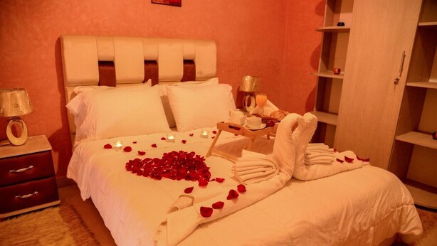 A neatly made bed with rose petals and towels, a bedside table with a lamp, and a wooden nightstand. - Hotel citta rossa (Marrakech)