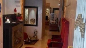 A hotel lobby with a red carpet, a chandelier, a reception desk, and red seating. - Hotel citta rossa (Marrakech)