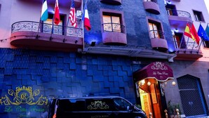 A hotel facade with balconies, flags, and a car parked in front. - Hotel citta rossa (Marrakech)
