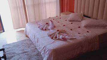 Habitación de hotel con cama, mesita de noche, una silla y ventana con cortinas.