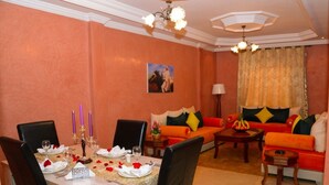 A dining area with a table set for four, a sofa, and a coffee table in a room with peach walls and a ceiling fan. - Hotel citta rossa (Marrakech)