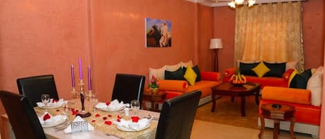 A dining area with a table set for four, a sofa, and a coffee table in a room with peach walls and a ceiling fan.