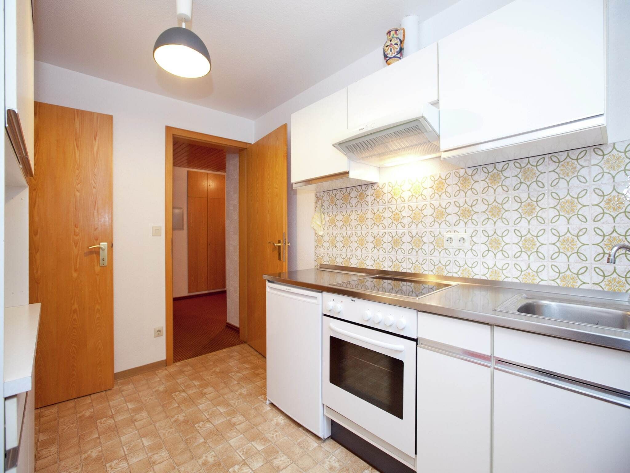 Cocina con armarios blancos, estufa y lavabo. Cuenta con un salpicadero decorado y una puerta de madera.