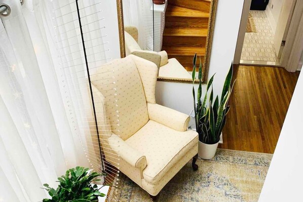 Un coin de pièce avec un fauteuil beige, une plante en pot et un miroir qui reflète un escalier.