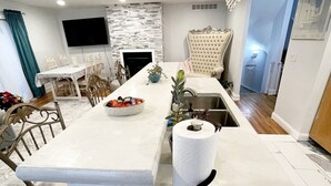 A modern kitchen with a marble countertop, a built-in sink, and a large island with a bowl of fruit.