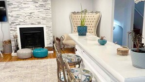 A modern living room with a fireplace, a sofa, a dining table with chairs, and decorative plants.