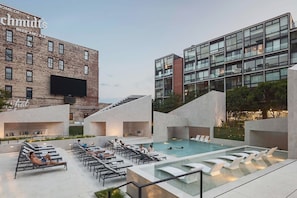 A rooftop pool area with lounge chairs and a swimming pool, surrounded by modern buildings with a sign that reads "Home of Schmidts Beer and Ale".