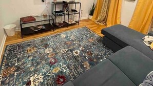 Un salon avec un téléviseur à écran plat fixé au mur, un meuble de rangement noir, un tapis à motifs, un canapé gris et des rideaux jaunes.