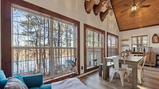 A spacious room with large windows, a cozy seating area, a dining table, and a kitchen area. - Sunset Escape, Waterfront, Sleeps 6, Fishing, 2 Kayaks, Games, + Firepit! (Eatonton)
