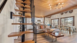A spacious living area with a wooden staircase, a sofa, a dining table, and a kitchen in the background. - Sunset Escape, Waterfront, Sleeps 6, Fishing, 2 Kayaks, Games, + Firepit! (Eatonton)