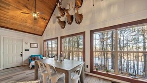 A spacious room with a wooden ceiling, large windows, a dining table with chairs, and a blue sofa. - Sunset Escape, Waterfront, Sleeps 6, Fishing, 2 Kayaks, Games, + Firepit! (Eatonton)