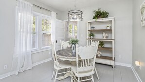 Un coin repas avec une table ronde, des chaises blanches, un lustre et une bibliothèque blanche agrémentée d’objets décoratifs.