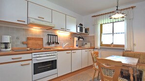 Une cuisine moderne avec des meubles blancs, un four encastré, une machine à café et un coin repas comprenant une table et des chaises.