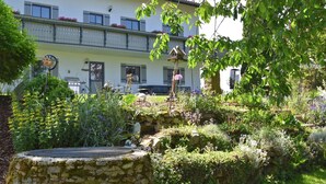 Un jardin avec un banc en pierre, une végétation luxuriante et, au fond, un bâtiment doté de balcons.