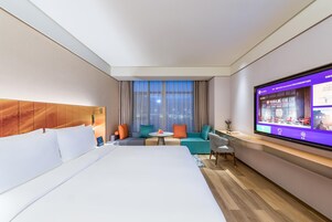 Habitación de hotel con una cama grande, zona de estar con una mesa y un televisor en la pared.
