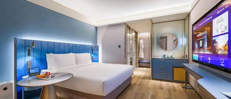 A modern hotel room with a bed, bedside table, TV, and a bathroom with a mirror.