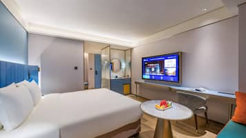 Habitación de hotel con cama, escritorio, televisión y una mesita con fruta.