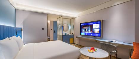 Habitación de hotel con cama, escritorio, televisión y una mesita con fruta.