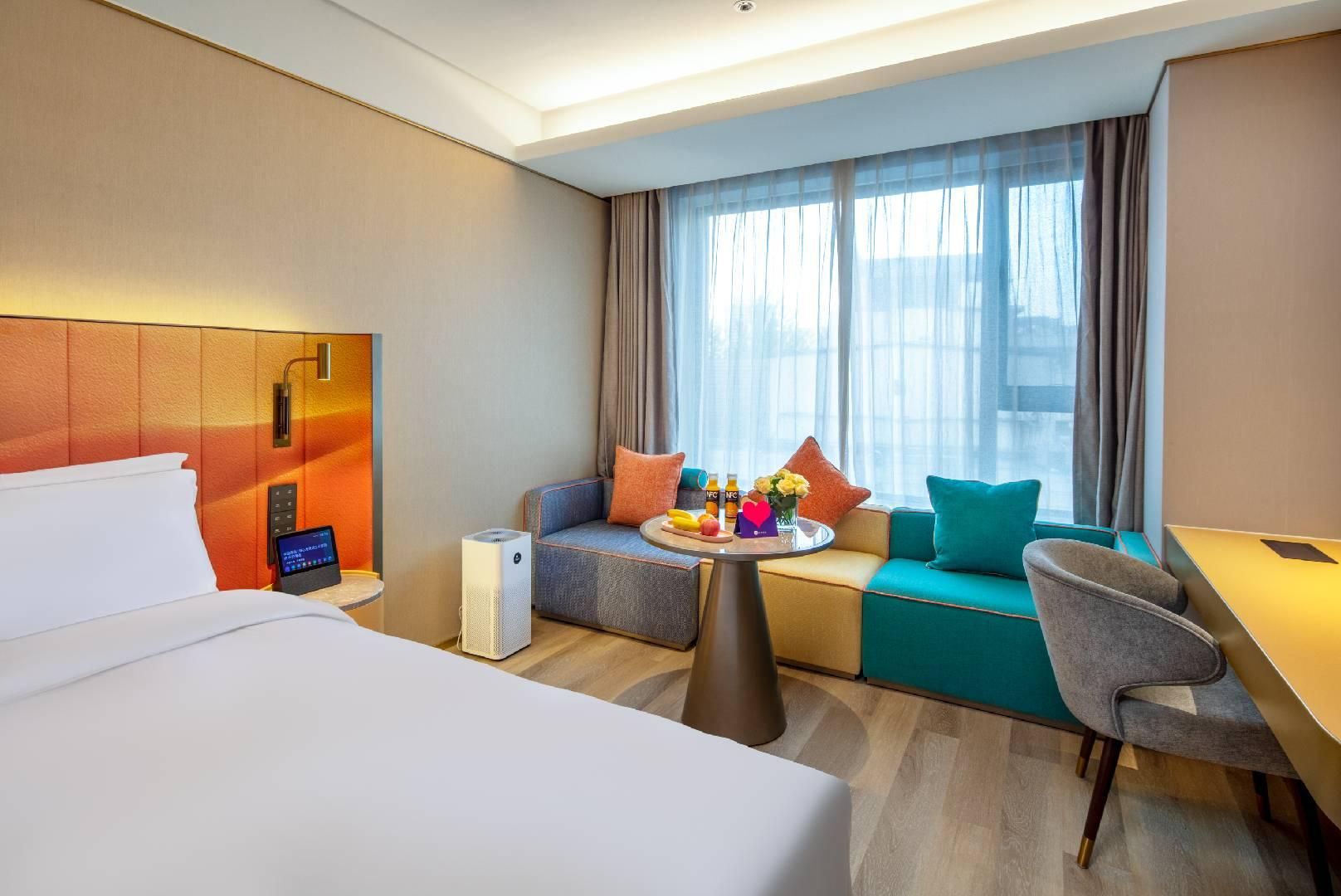 Et hotelværelse med en seng, en sofa, et lille bord med frugt og drikkevarer samt et skrivebord.
