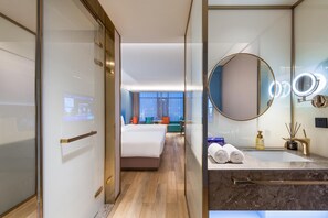 A hotel room with a bed, a seating area with a view, a bathroom with a mirror and toiletries.