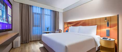 Una habitación de hotel con una cama grande, una mesita de noche con lámpara, un televisor a la izquierda y una ventana con cortinas.
