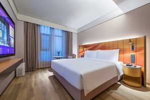 A modern hotel room with a large bed, a desk, a TV, and a view of the outdoors.