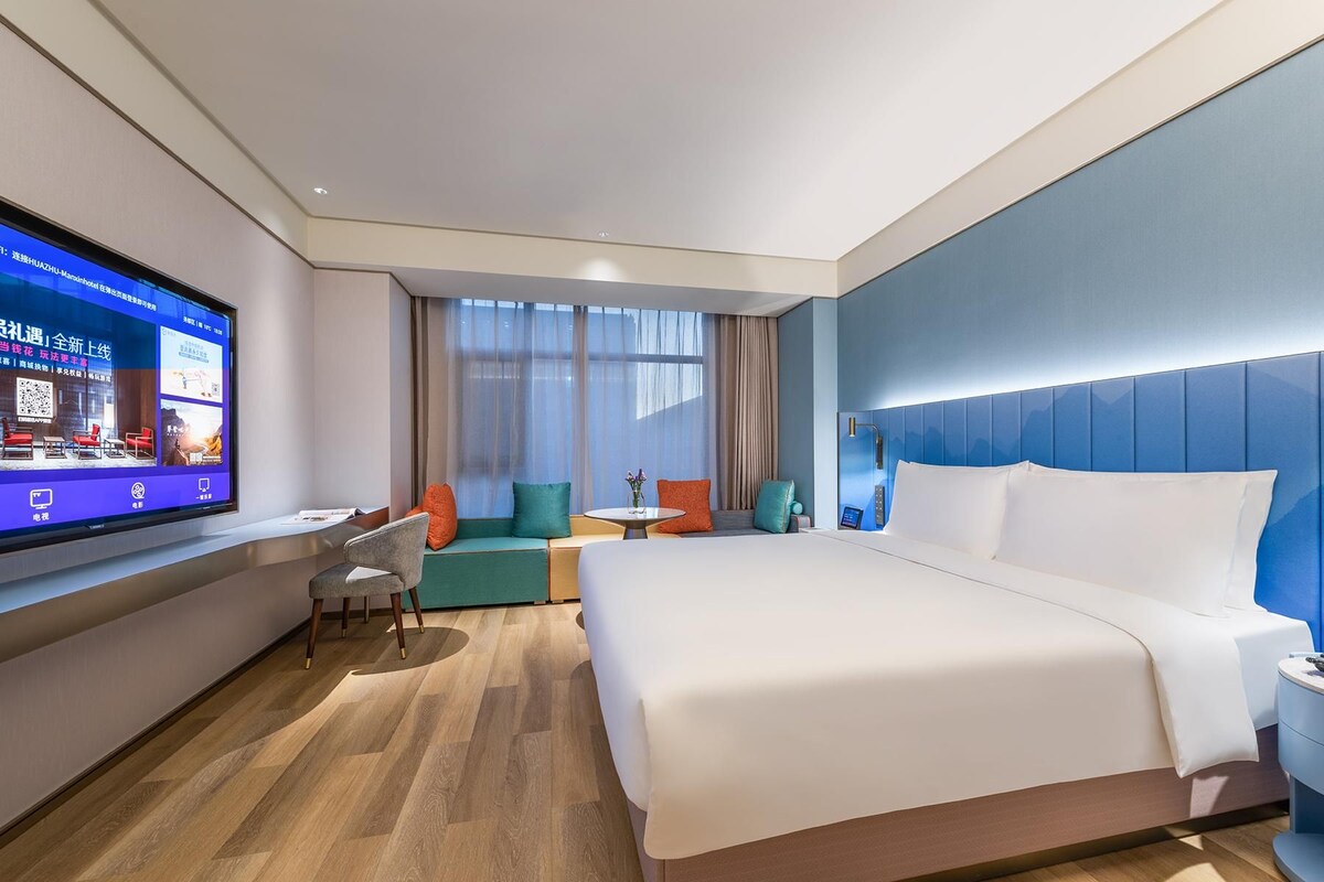 A modern hotel room with a large bed, a desk, and a TV.