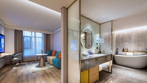 A modern hotel room with a large window, a sofa, a round table, a TV, a bathroom with a bathtub, and a vanity with a mirror. - Manxin Hotel Linfen Yingbin Avenue (Linfen)