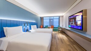 Habitación de hotel con dos camas, un televisor en la pared y zona de estar con vista a la ciudad.