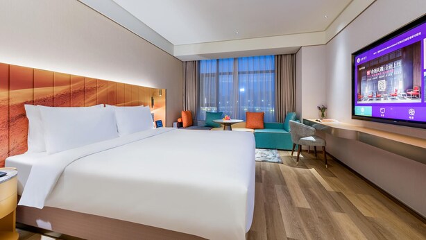 Una habitación de hotel moderna con una cama grande, un área de descanso con una mesa y un televisor en la pared.