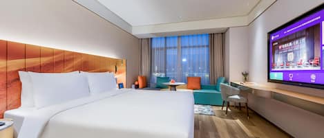 Una habitación de hotel moderna con una cama grande, un área de descanso con una mesa y un televisor en la pared.