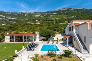 Un espace piscine doté d’une terrasse en pierre, de chaises longues et offrant une vue sur un paysage montagneux.