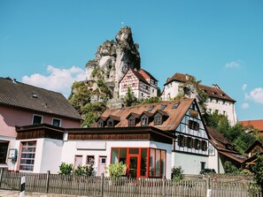 Ein traditionelles Fachwerkhäuschen mit roter Tür, heller Fassade und Blick auf einen felsigen Berg im Hintergrund.