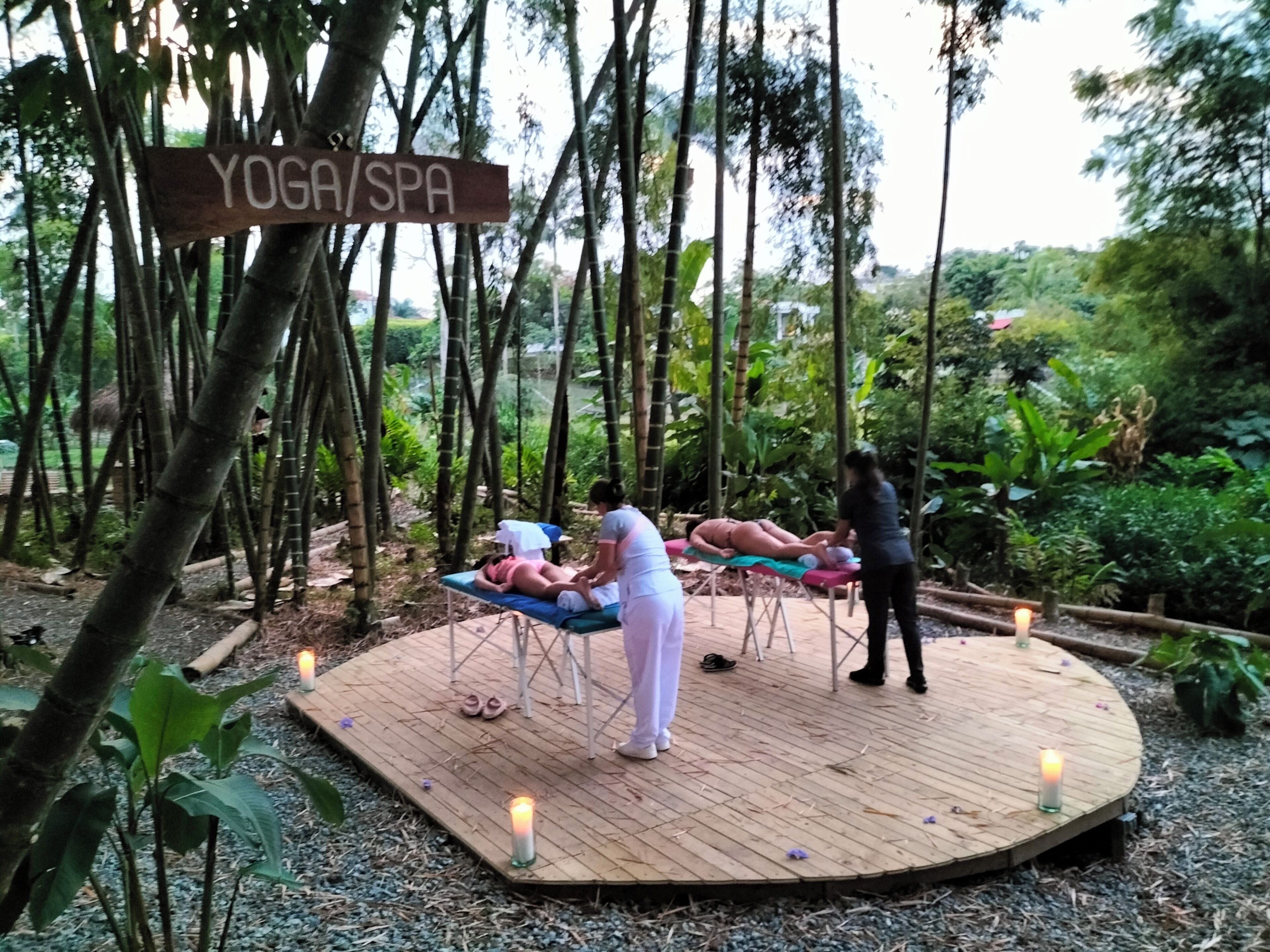 Een houten platform met twee massagetafels en een bordje met de tekst 'YOGA/SPA'.