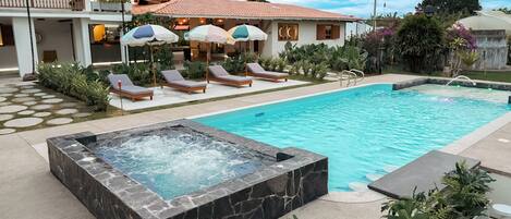 A swimming pool with a hot tub, sun loungers, and umbrellas.