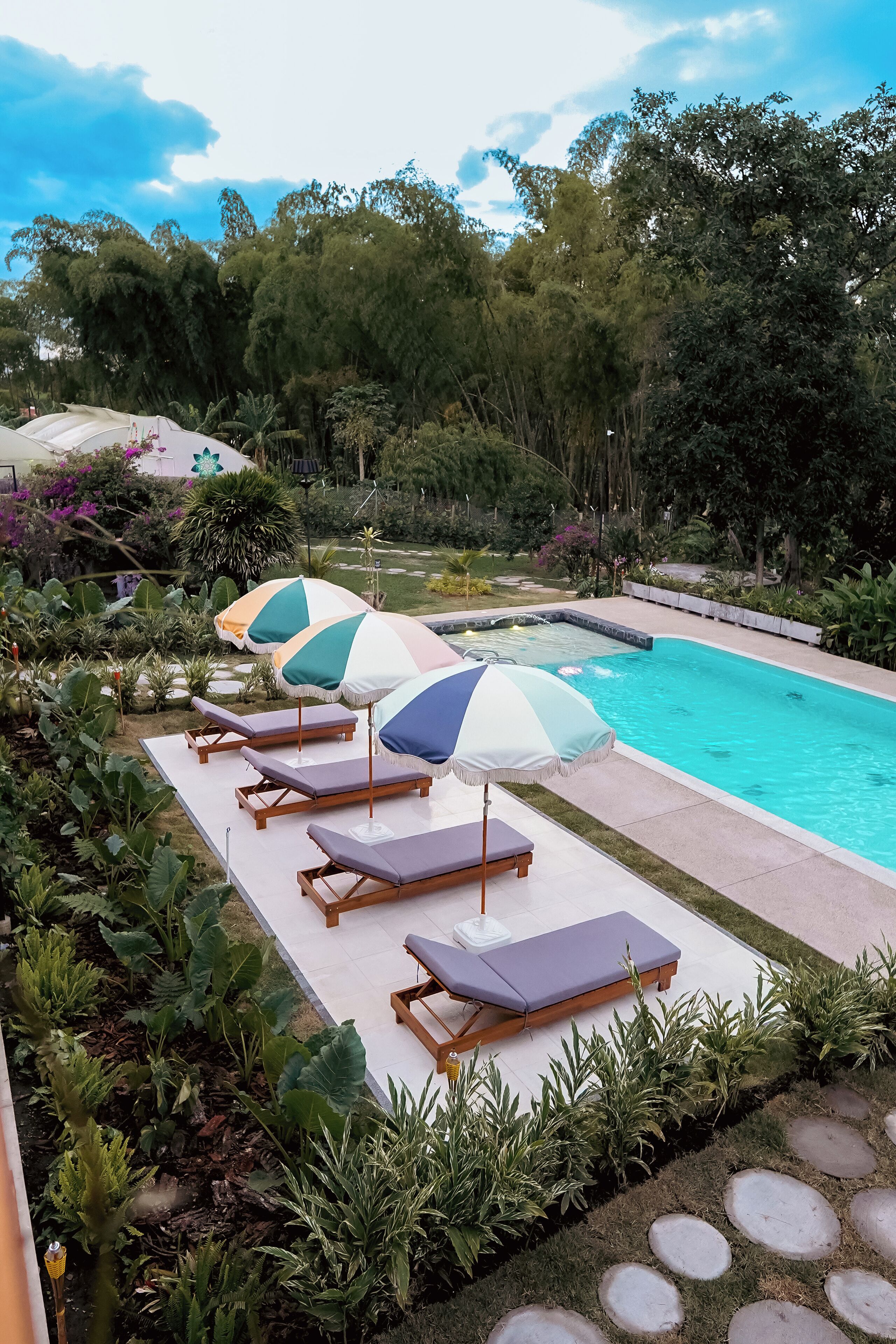 Ein Poolbereich mit Liegestühlen und Sonnenschirmen, umgeben von üppiger Vegetation.