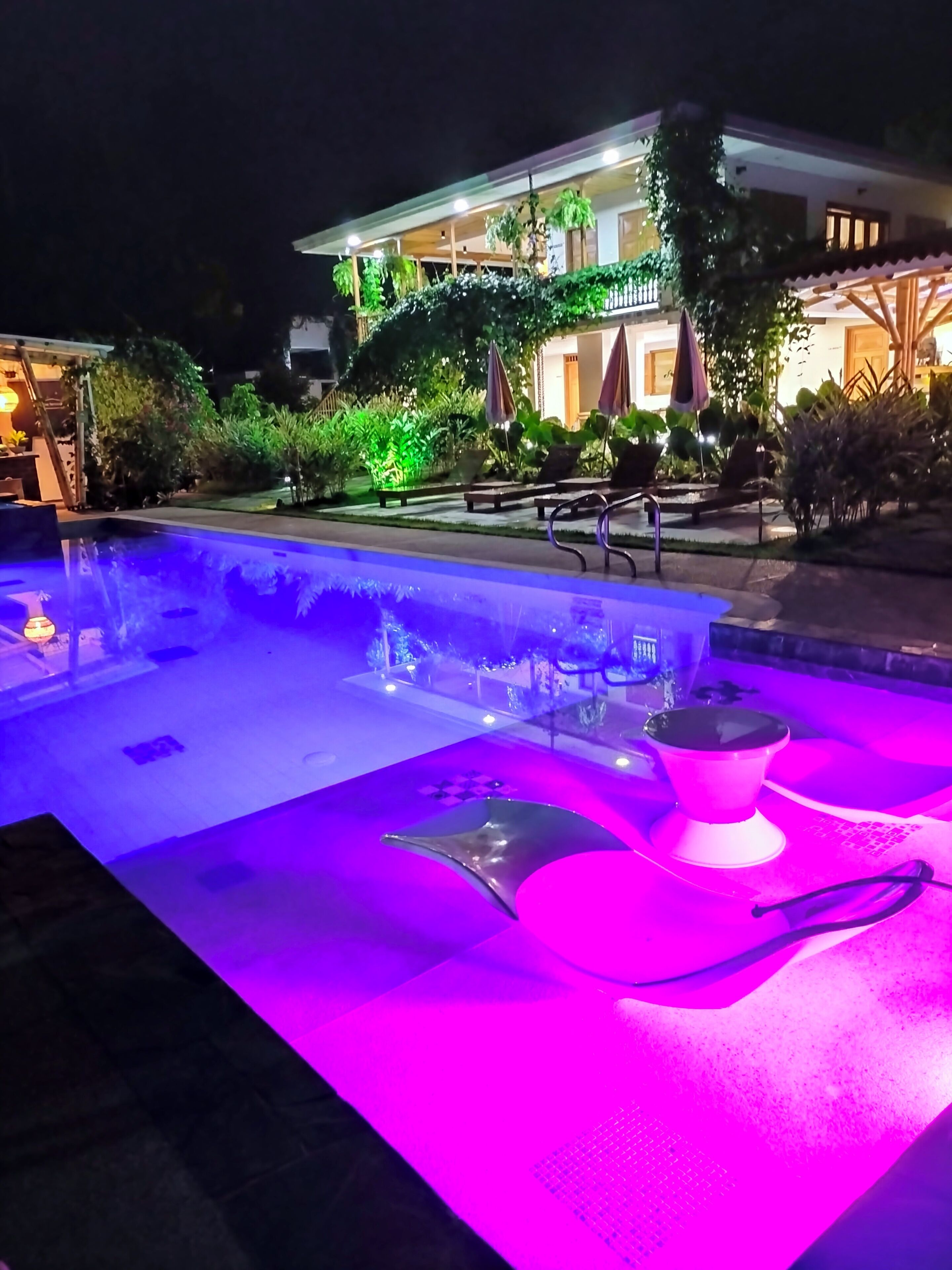 Una piscina con una fuente de agua y un edificio iluminado al fondo.