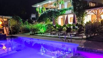Una piscina con una fuente de agua y un edificio iluminado al fondo.