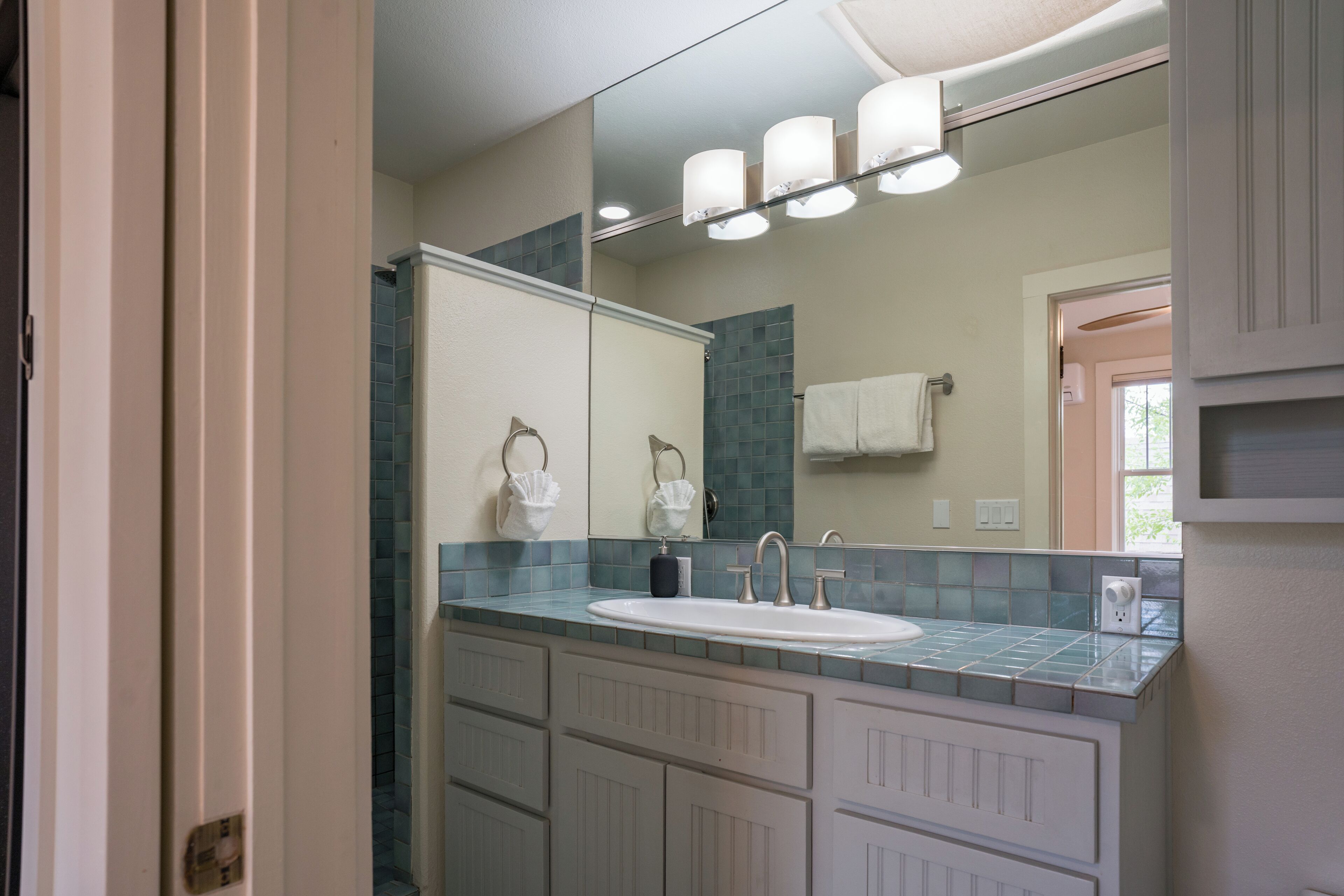 A bathroom with a large mirror, a sink, and a vanity with cabinets.