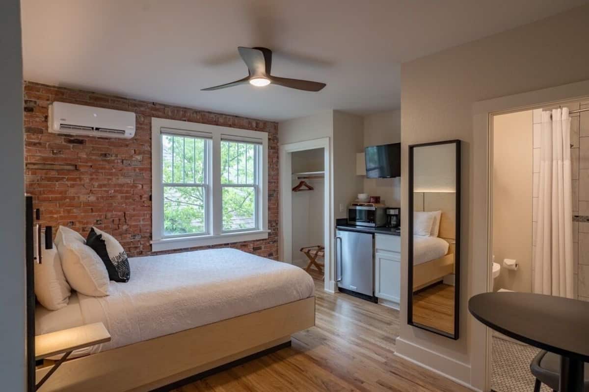 A bedroom with a bed, a ceiling fan, a brick wall, and a window.