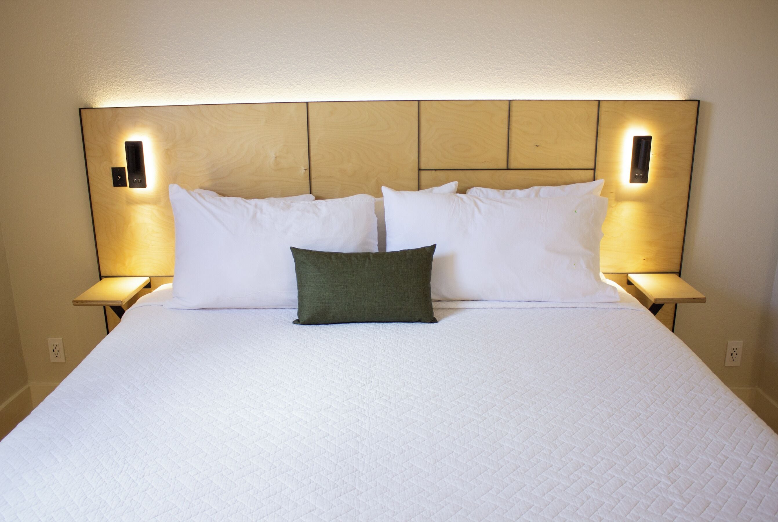 Una cama bien hecha con cubrecolcha blanco acolchado, dos lámparas de noche y un cabecero de madera.