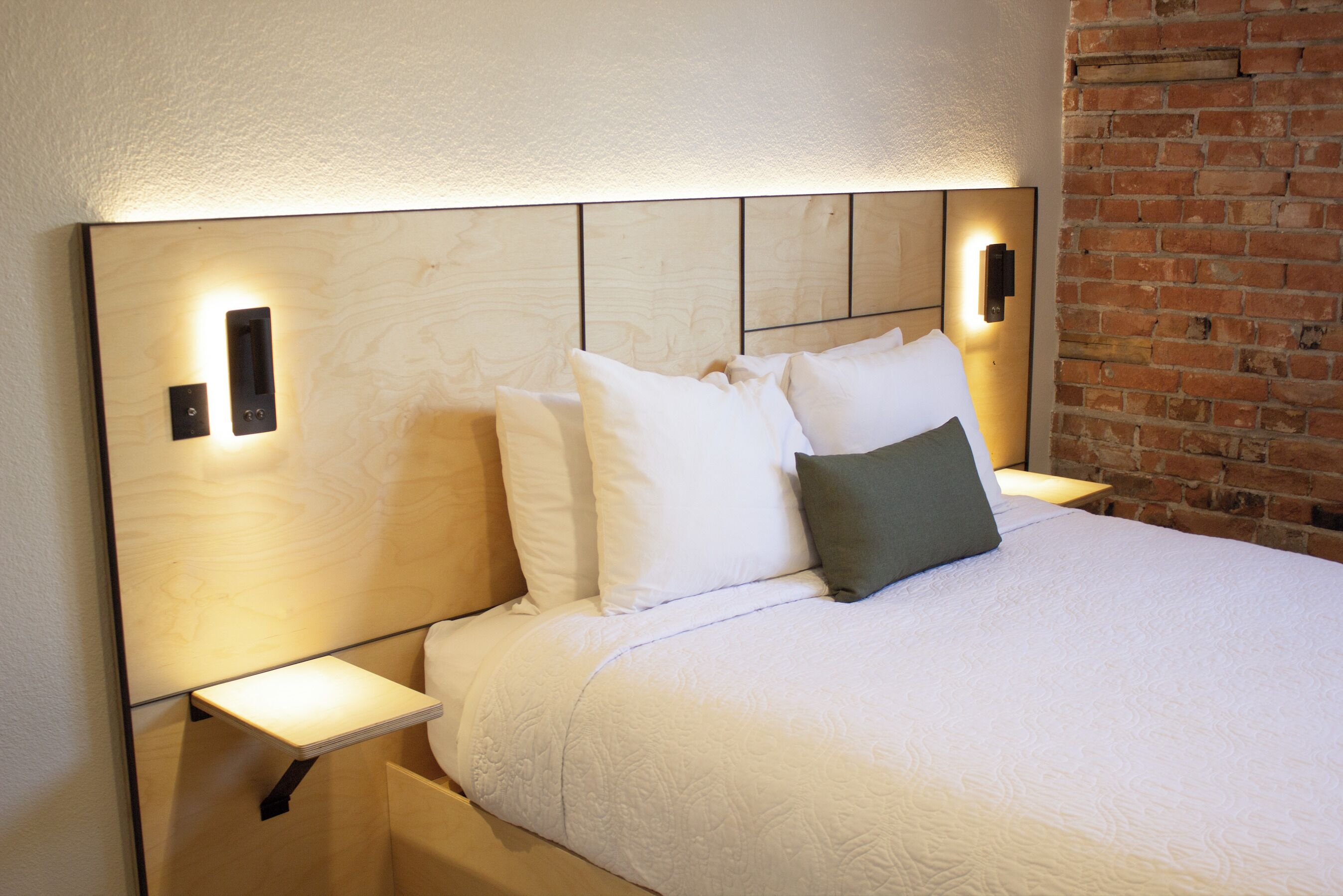 A neatly made bed with white bedding and a grey pillow, flanked by bedside tables with wall-mounted lamps.