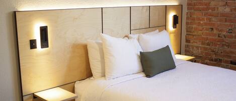 A neatly made bed with white bedding and a grey pillow, flanked by bedside tables with wall-mounted lamps.