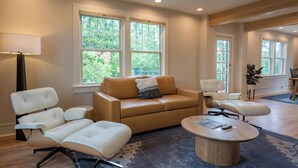 A modern living room with a beige sofa, white armchairs, and a round coffee table. - Leland House Suites of Durango (Durango)