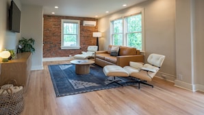 A modern living room with a brick wall, leather sofa, and a flat-screen TV. - Leland House Suites of Durango (Durango)