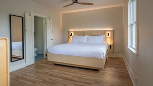 A bedroom with a bed, a ceiling fan, bedside lamps, a mirror, and a window. - Leland House Suites of Durango (Durango)