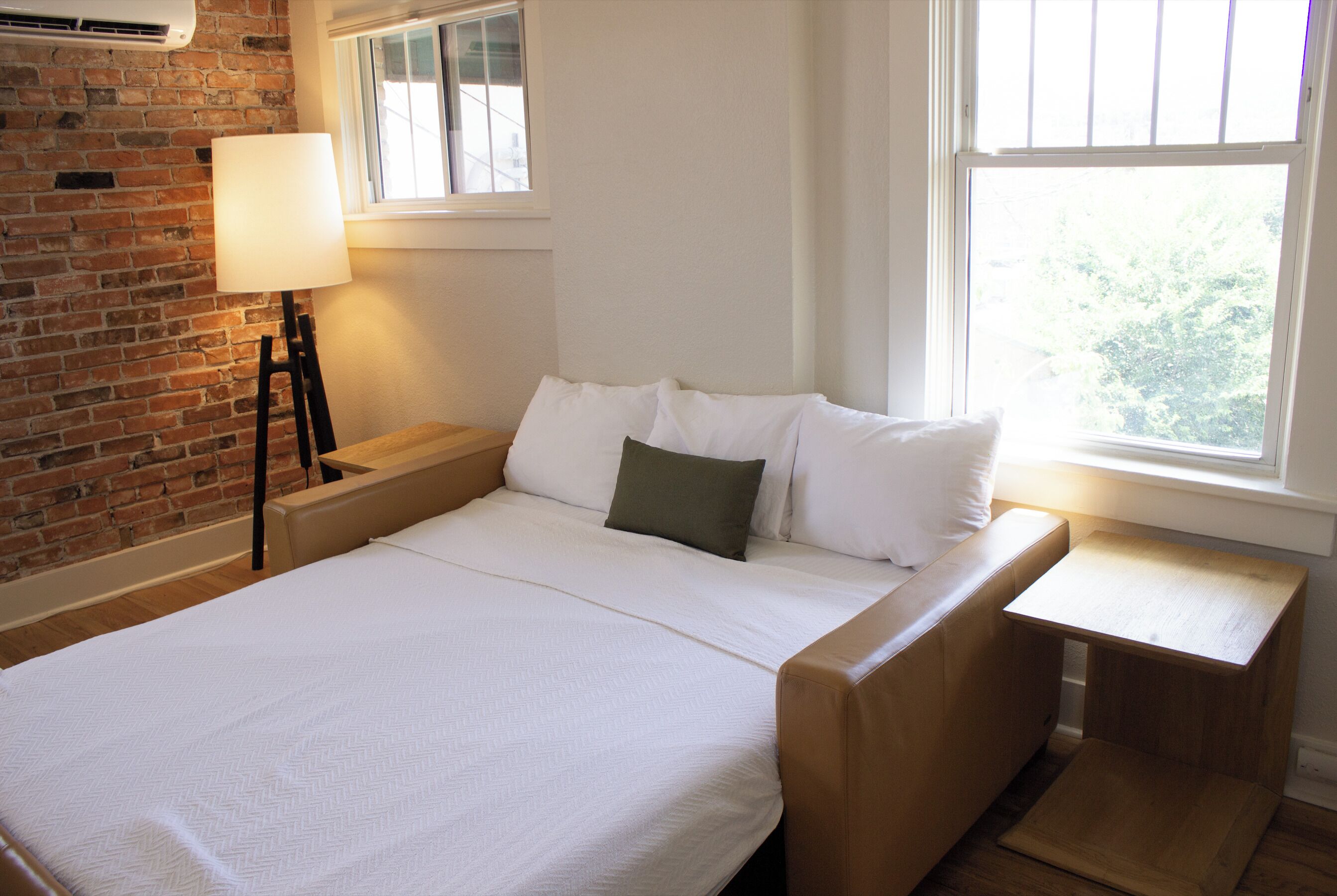 Een slaapkamer met een bakstenen muur, een raam, een nachtkastje en een bed met witte beddengoed.