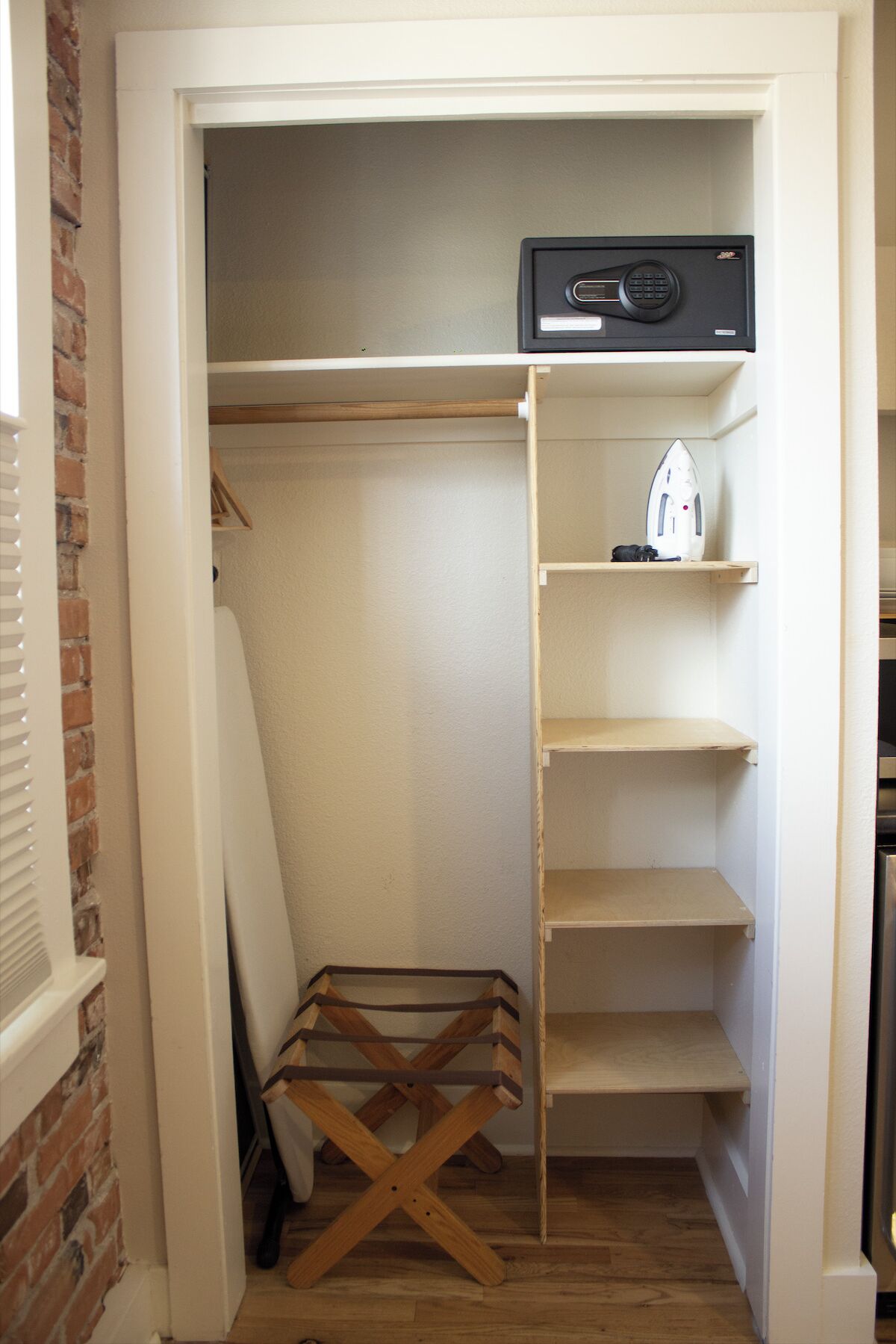 A walk-in closet with a hanging rod, shelves, and a small ironing board.